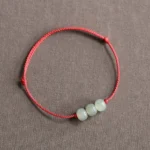 Three light cyan jade beads on red braided cord bracelet, flat lay top-down view