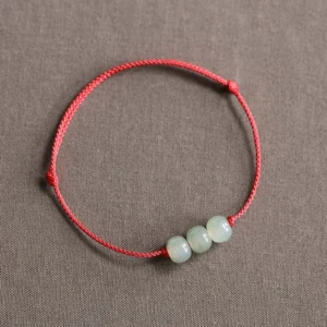 Three light cyan jade beads on red braided cord bracelet, flat lay top-down view
