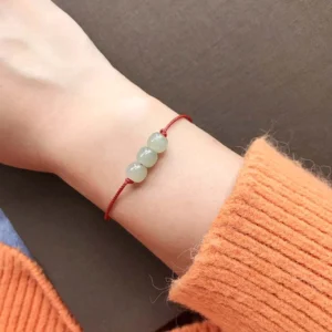 Three jade beads red string bracelet worn on wrist with orange knit sweater, lifestyle wearing view