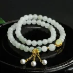 Tianshan jade lotus gourd prosperity bracelet double loop with gold lotus charm and pearl tassel pendant, overhead view on black tray