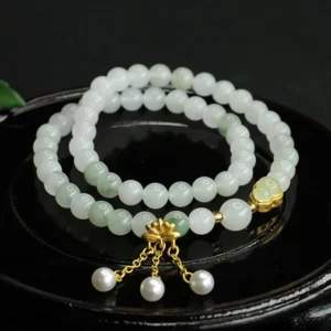 Tianshan jade lotus gourd prosperity bracelet double loop with gold lotus charm and pearl tassel pendant, overhead view on black tray