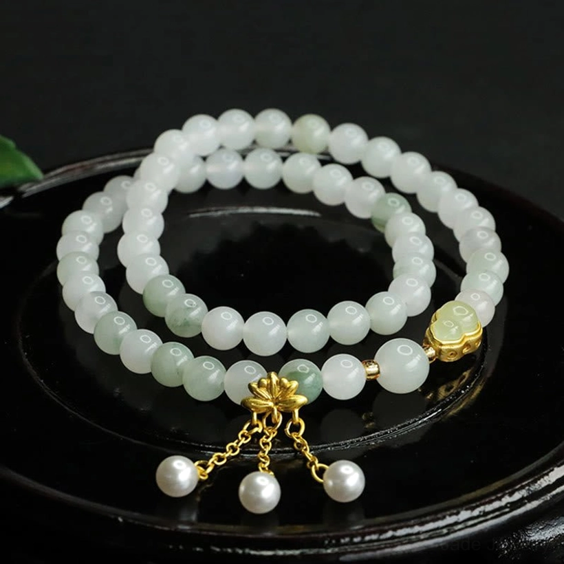 Tianshan jade lotus gourd prosperity bracelet double loop with gold lotus charm and pearl tassel pendant, overhead view on black tray