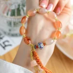 Tibetan candy agate jade strength bracelet worn on wrist with gold metal spacers and decorative tassel