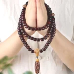 Hand-held 108 mala bead bracelet with three-eye Dzi bead, jade stones, and bodhi seeds displaying authentic Tibetan spiritual craftsmanship