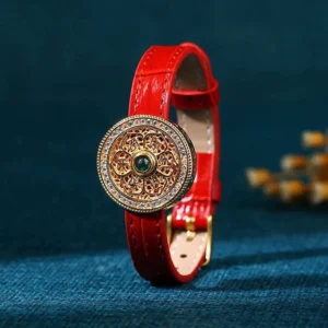 Om Mani Padme Hum red jade leather bracelet with gold-plated Eight Treasures compass charm and central green jade stone on dark blue backdrop