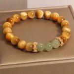 Tiger Eye and Jade courage bracelet with pearl-adorned gold spacers on brown display tray - overhead flat lay view showing warm golden tiger eye beads and pale green jade stones
