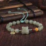 Tiger zodiac jade blessing bracelet with adjustable drawstring and gold charm pendant, overhead view on bamboo and dark wood background