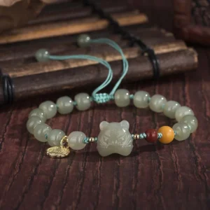 Tiger zodiac jade blessing bracelet with adjustable drawstring and gold charm pendant, overhead view on bamboo and dark wood background