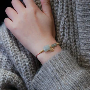 Tiger jade red string protection bracelet worn on wrist with gray knit sweater, showing subtle styling and gold accents