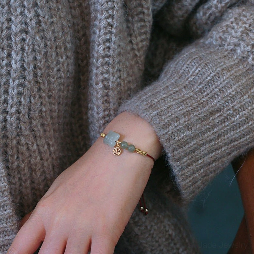 Low-angle side view of tiger jade red string bracelet on wrist showing full bracelet design with gold charm and knit sweater background