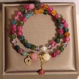 Colorful tourmaline bead bracelet with copper coin charm and red gemstone pendant on display tray