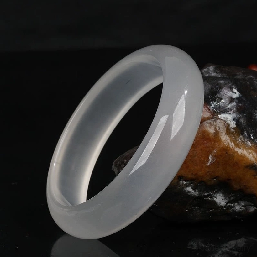 Single translucent white jade bangle in side oblique view with milky white glossy texture on dark backdrop