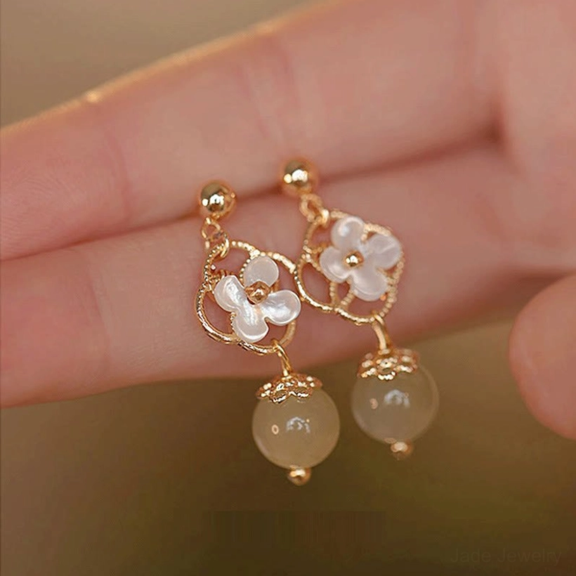 Jade drop earrings worn on ear, profile view showing tridacna floral design and jade bead in hand-touching-hair styling moment