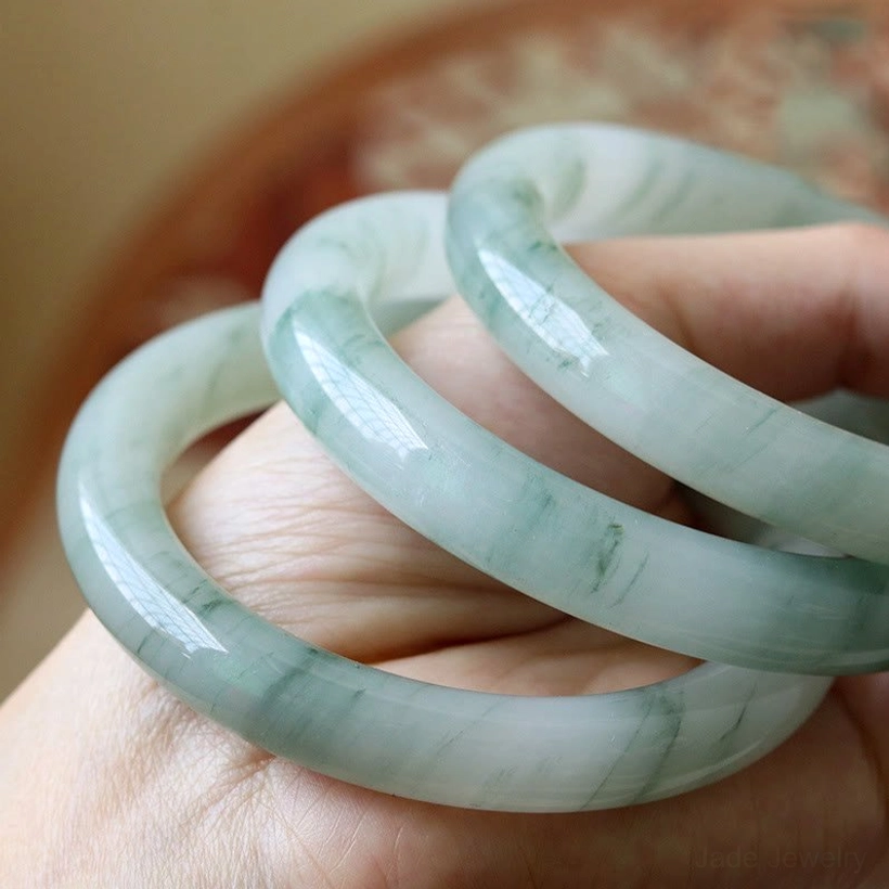 Three natural jade prosperity bangles held together in hand showing consistent green marbled jade design and perfect roundness