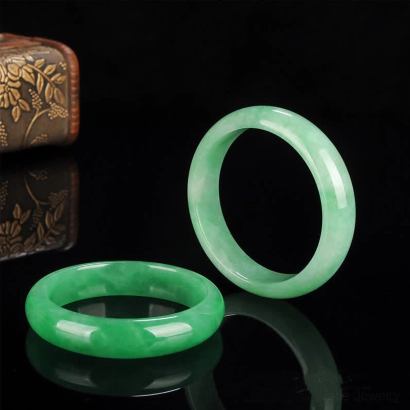 Two natural jade bangle bracelets in different shades displayed together, one deep green and one light green, showing color variation range