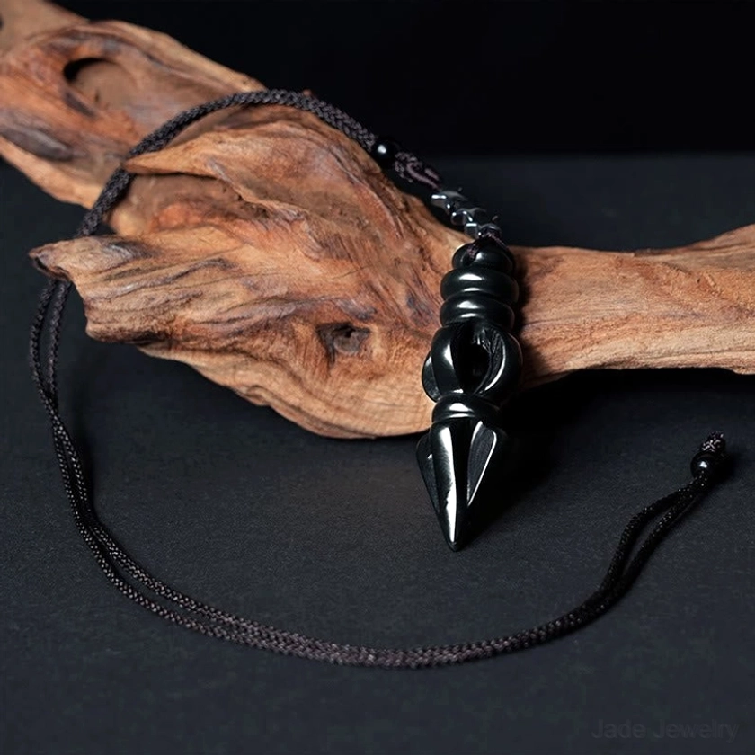 Vajra Dorje pendant necklace laid flat on driftwood with fully extended black woven cord displaying complete pendant surface details