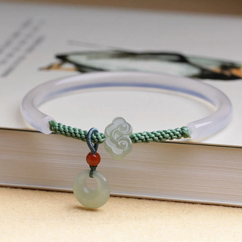 White agate and Hetian jade peace buckle bracelet flat lay on book, showing translucent agate bangle with jade charm pendants