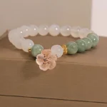 White agate jade flower charm bracelet with milky white beads and green jade accents displayed on brown jewelry box