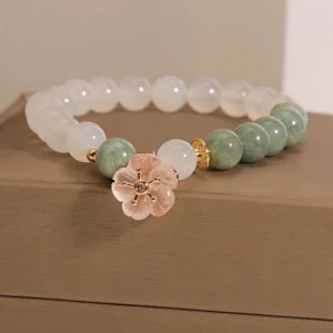 White agate jade flower charm bracelet with milky white beads and green jade accents displayed on brown jewelry box