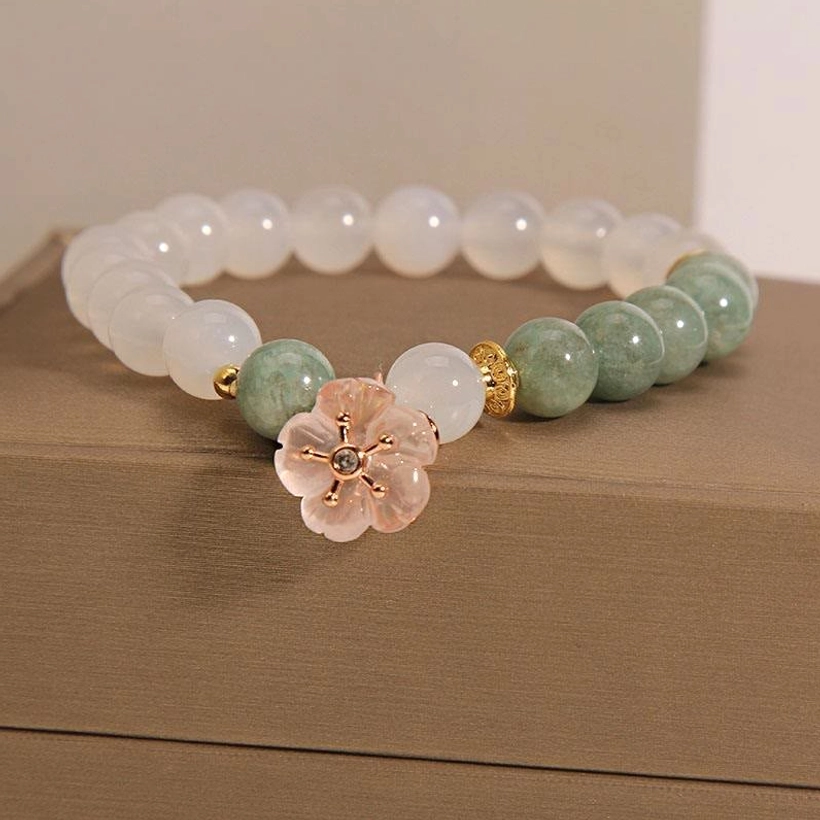 White agate jade flower charm bracelet with milky white beads and green jade accents displayed on brown jewelry box