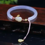 White agate hetian jade rabbit bracelet bangle with pink braided cord and golden gourd charm on wooden surface