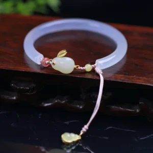 White agate hetian jade rabbit bracelet bangle with pink braided cord and golden gourd charm on wooden surface