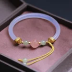 White agate lotus jade bangle bracelet with pale lavender agate, carved pink lotus centerpiece, and gold metal accents displayed on dark jewelry box lining