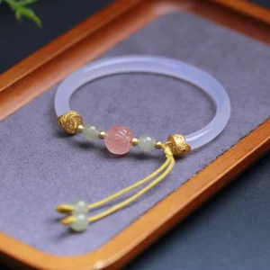 Angled view of jade lotus bangle showing decorative yellow tassel with jade beads and intricate lotus carving on light gray fabric