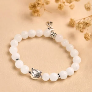 Flat lay view of white chalcedony cat charm bracelet with silver cat head charm and dried flowers on stone backdrop