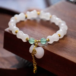 White golden silk jade bamboo bracelet with green aventurine beads and gold Fu character charm pendant displayed on wooden surface