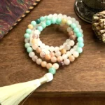 108 white jade and amazonite mala beads bracelet with white tassel flat lay on wooden surface showing natural stone bead texture and color variations