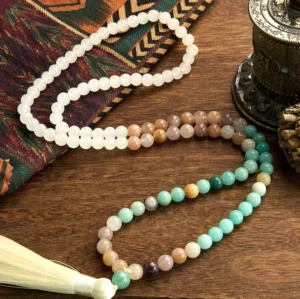 Two 108 mala bead bracelets with white jade and amazonite stones paired with white tassels displayed on patterned cloth wooden table for gift presentation