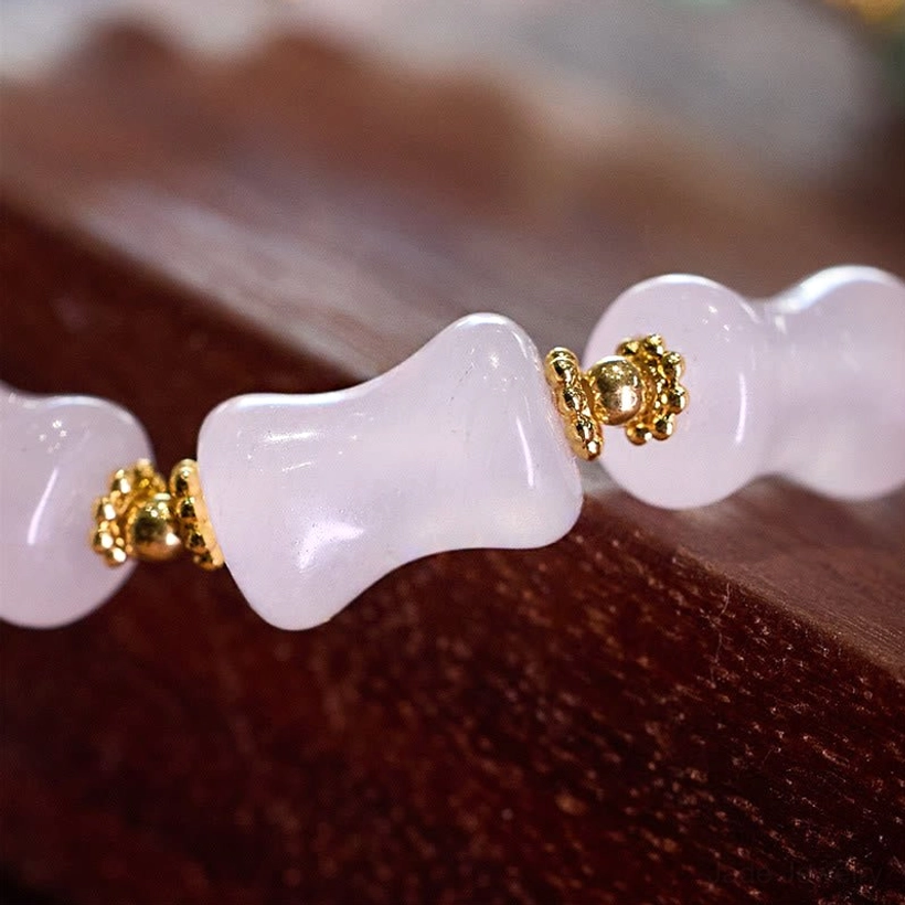 Extreme close-up of polished white bamboo jade beads and gold metal connectors on elastic cord bracelet
