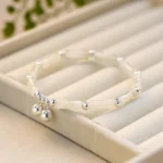 White jade bamboo bell sterling silver bracelet with double silver charms displayed on beige jewelry tray - flat lay top view