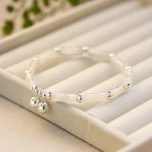 White jade bamboo bell sterling silver bracelet with double silver charms displayed on beige jewelry tray - flat lay top view