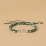 Green and white woven white jade bamboo bracelet with reincarnation knot and silver tassel on flat lay display