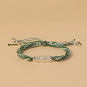 Green and white woven white jade bamboo bracelet with reincarnation knot and silver tassel on flat lay display