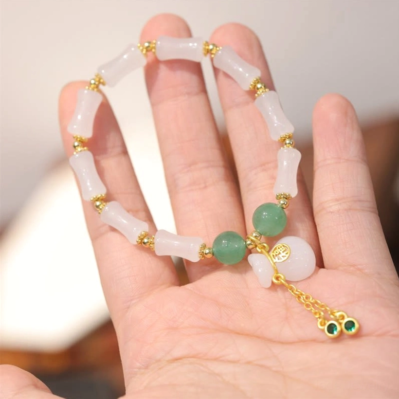 Hand-held view of white golden silk jade bracelet with clear bead arrangement, green aventurine spacers, and Fu tassel charm