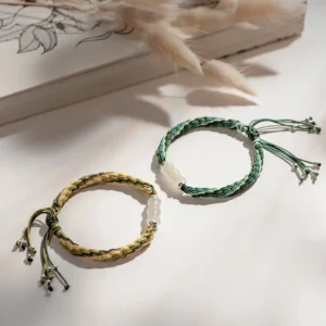 Two adjustable white jade bamboo string bracelets with reincarnation knots displayed on book with dried plants styling