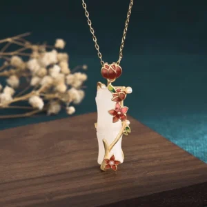 White jade bamboo lotus necklace with red enamel flowers and gold metal accents, front view on rustic wooden surface