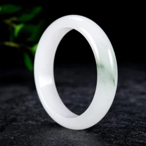 White jade bangle with subtle green streaks in three-quarter perspective displaying smooth glossy surface and authentic stone texture