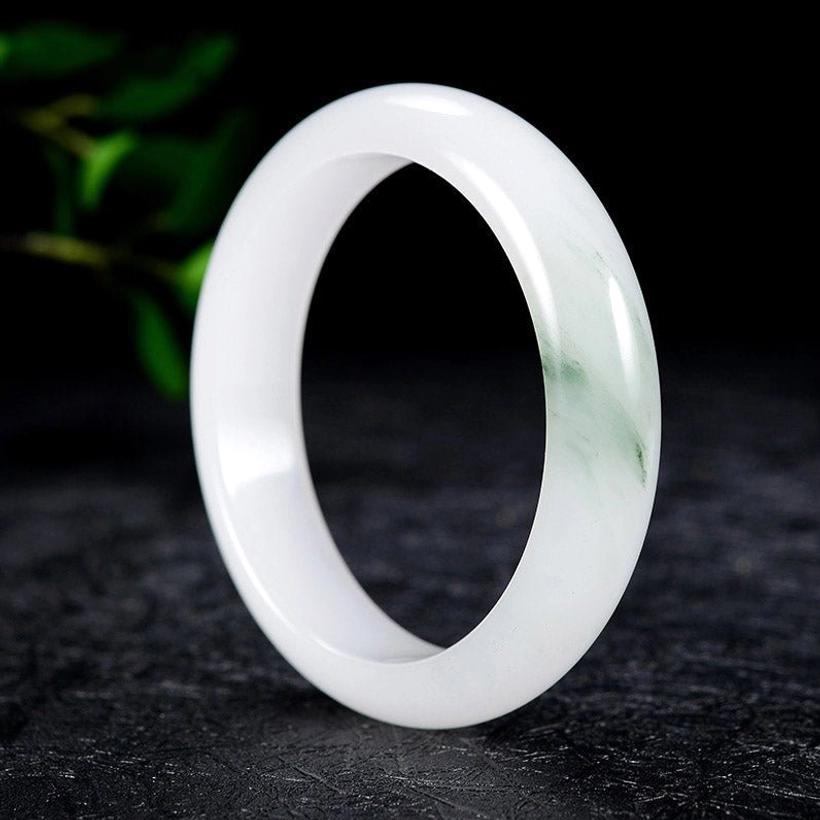 White jade bangle with subtle green streaks in three-quarter perspective displaying smooth glossy surface and authentic stone texture