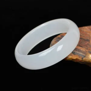 Translucent white Xinjiang golden silk jade bangle bracelet with natural luminosity, displayed on weathered wood with black background