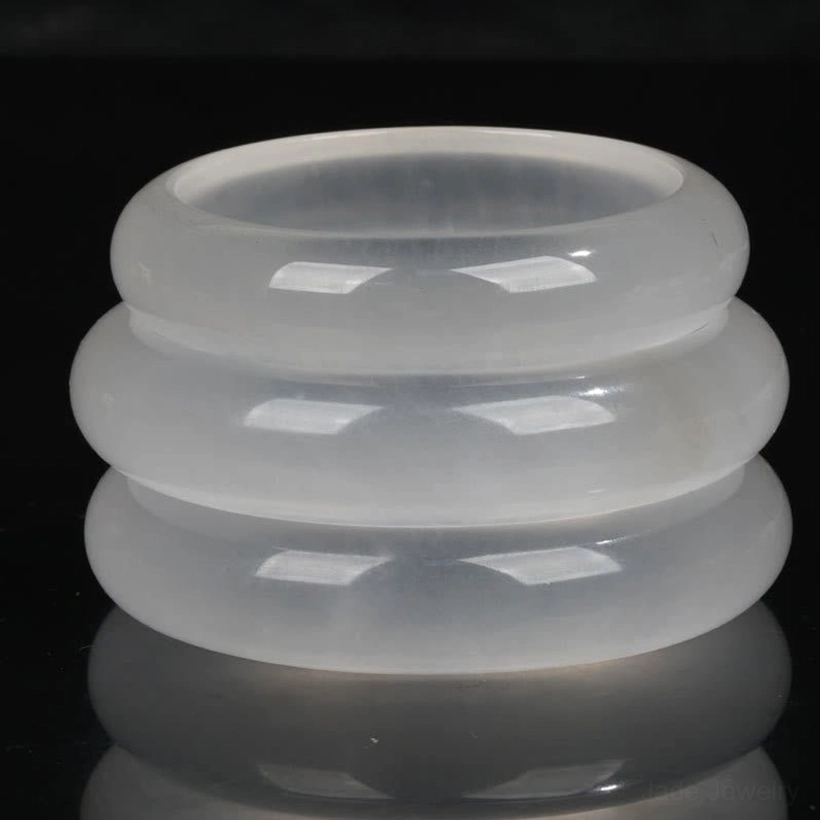 Stacked golden silk jade bangles in top-down flat lay showing uniform milky white translucent design on dark studio background