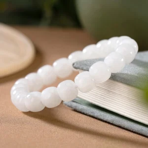 Close-up oblique angle of glossy white jade barrel beads bracelet on stacked books with warm ambient lighting