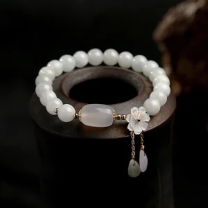 Natural white jade beaded bracelet with delicate shell flower charm and stone teardrop pendants on display stand