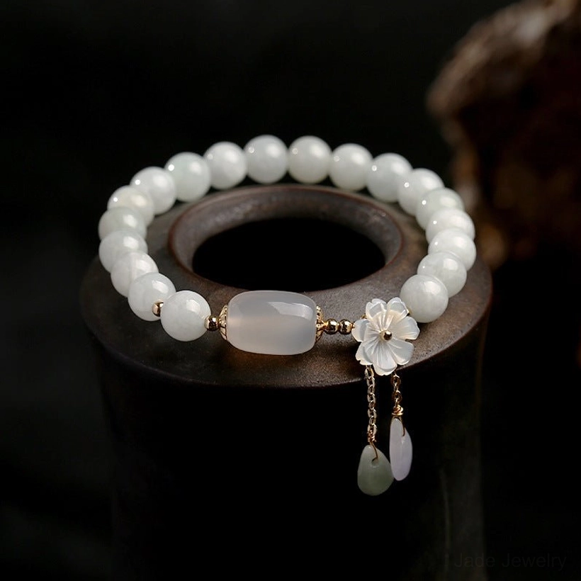 Natural white jade beaded bracelet with delicate shell flower charm and stone teardrop pendants on display stand