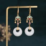 White jade blessing drop earrings with gold-tone metal and enamel accents, frontal view on display stand