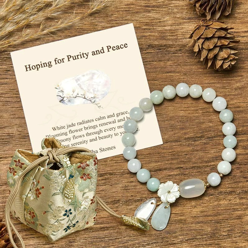 White jade purity bracelet with flower charm and teardrop pendants in silk embroidered gift pouch on wooden table