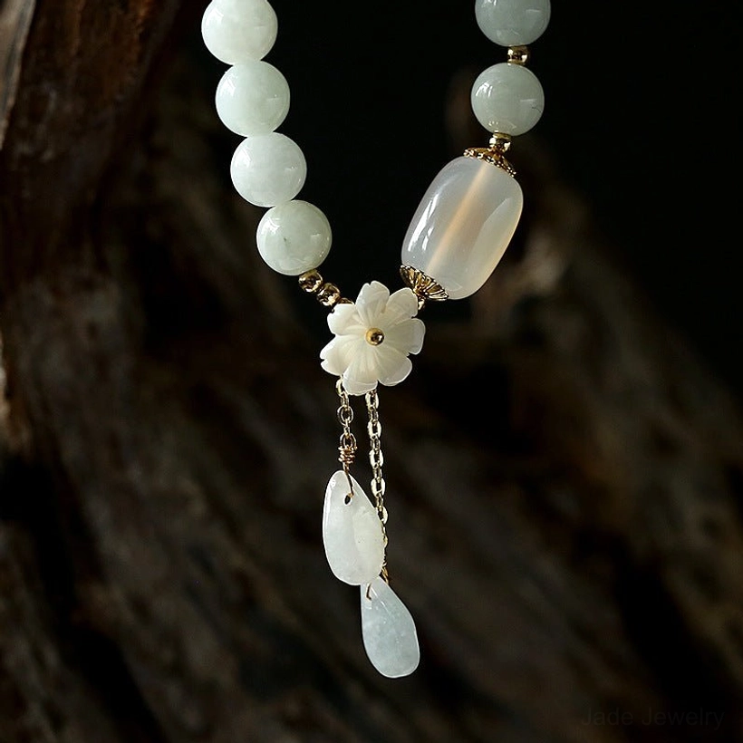 Long strand white jade beaded bracelet with large barrel bead, shell flower charm, and dangling teardrop stone charms